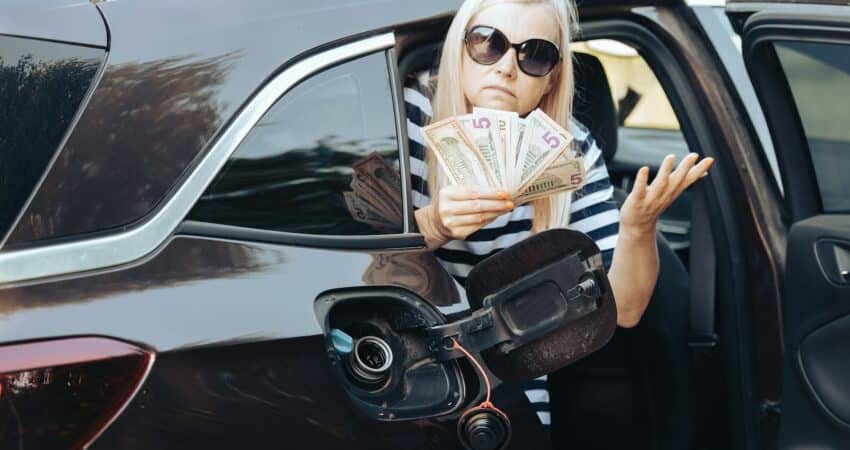 desperate woman hold cash dollar bills in to car with an open tank, concept of rising fuel prices